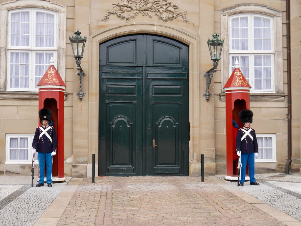 Two guards in uniform standing outside red guard boxes, in front of the Amalienborg Palace, Copenhagen.