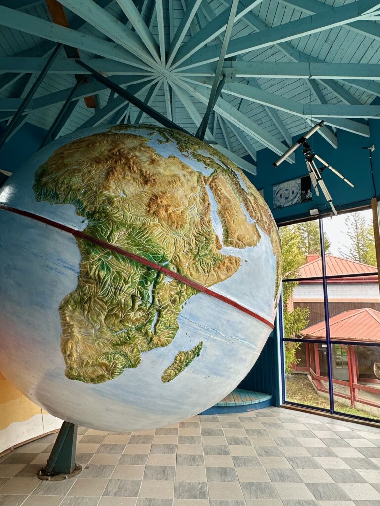 A giant rotating globe set on an angle, inside a small building with an intricate wooden roof and a tiled floor.  The building is fully accessible through a wide doorway.