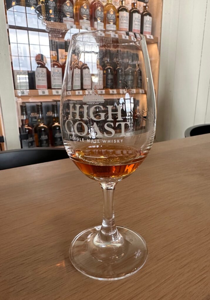 A glass containing whisky with a selection of whisky bottles in the background.