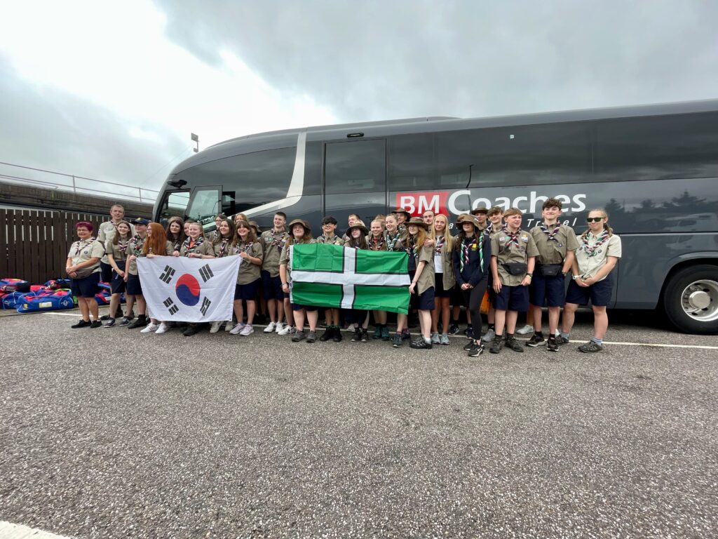 All of the Unit 78 Scouts attending the Jamboree waiting to bard the coach.  They are holding a Devon flag and Korean flag.