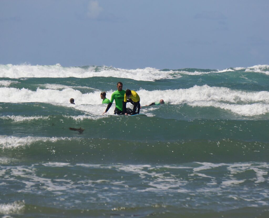 Image shows Stan on the surf board and half way to his feet.  Cyril is sitting on the back of the board.