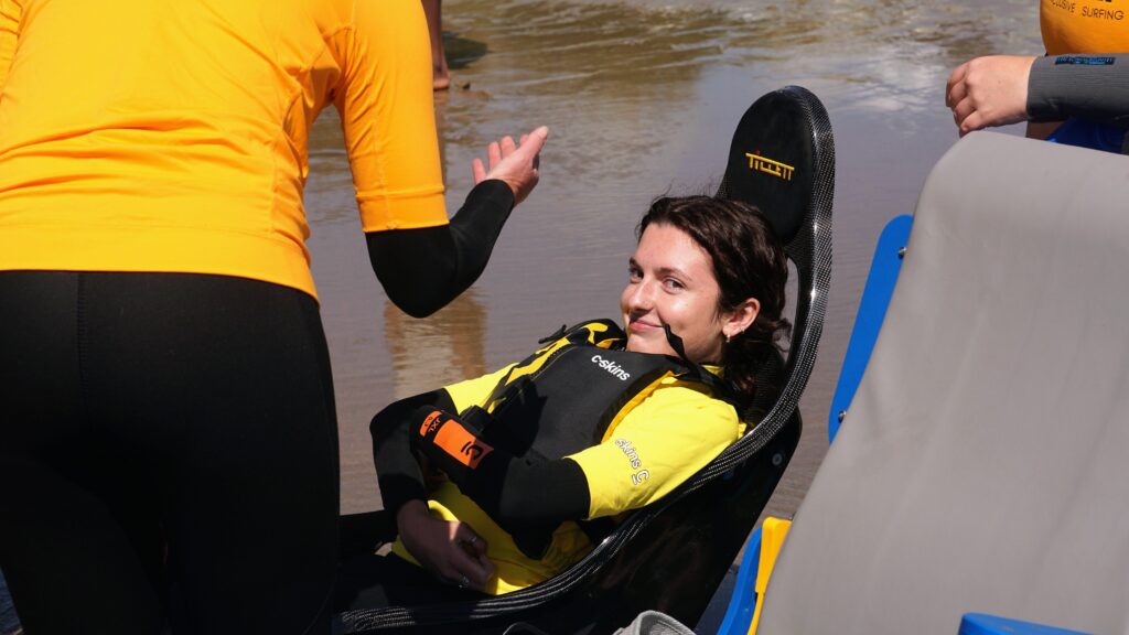 Image shows Molly on the adaptive surfing board and smiling, although looking a little nervous