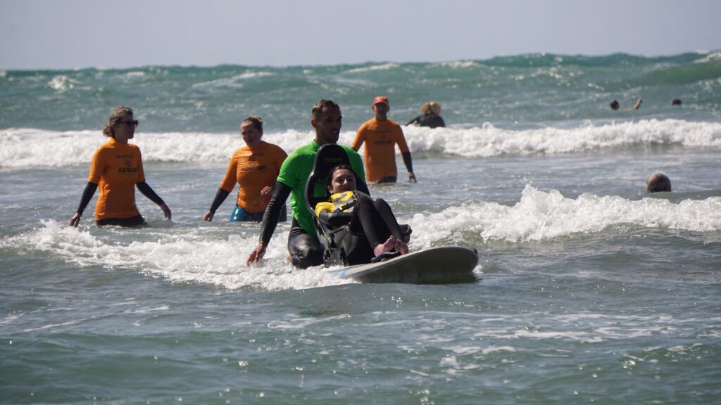 Using the adaptive surfing board - image shows Molly and Cyril in the water with three volunteers standing behind