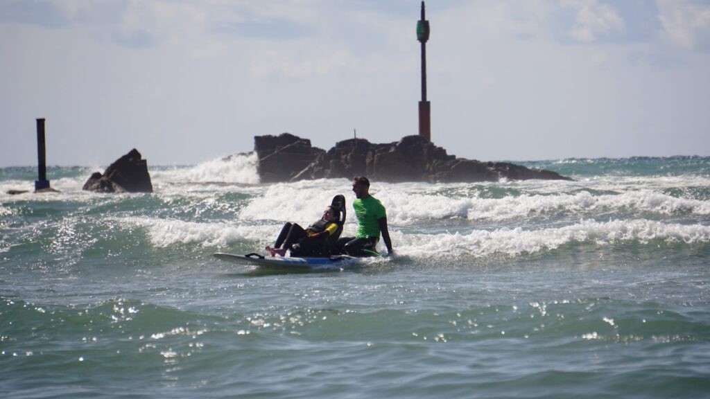 Using the adaptive surfing board - image shows Molly in the chair while Cyril is guiding the board from behind
