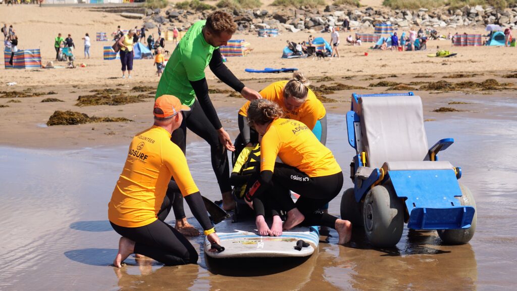 Image shows Cyril and the volunteers securing Molly into the adaptive surfing board