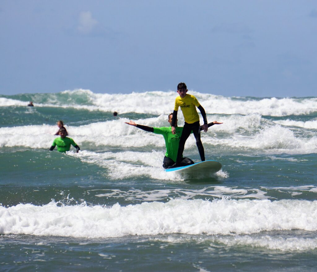 Image shows Stan on his feet on the surf board and Cyril holding his arms out wide to show that he is not helping him at this moment