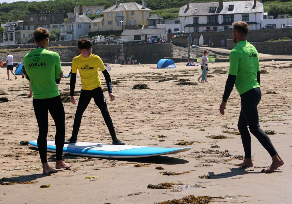 Image shows the instructors giving a preparatory lesson on the beach and Stan practising his pose