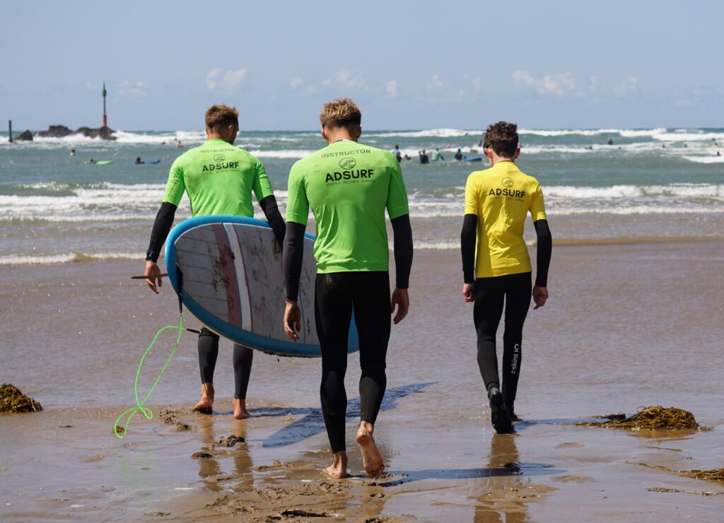 Image shows two instructors and Stan walking into the sea. One is carrying a surf board.