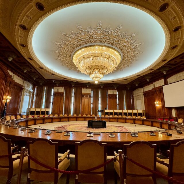 Picture shows the Hall of Human Rights in the Palace of Parliament. There are sixty seats mourn a circular table and the edge of the room. There is also a huge chandelier weighing two and a half tonnes, suspended from the ceiling.