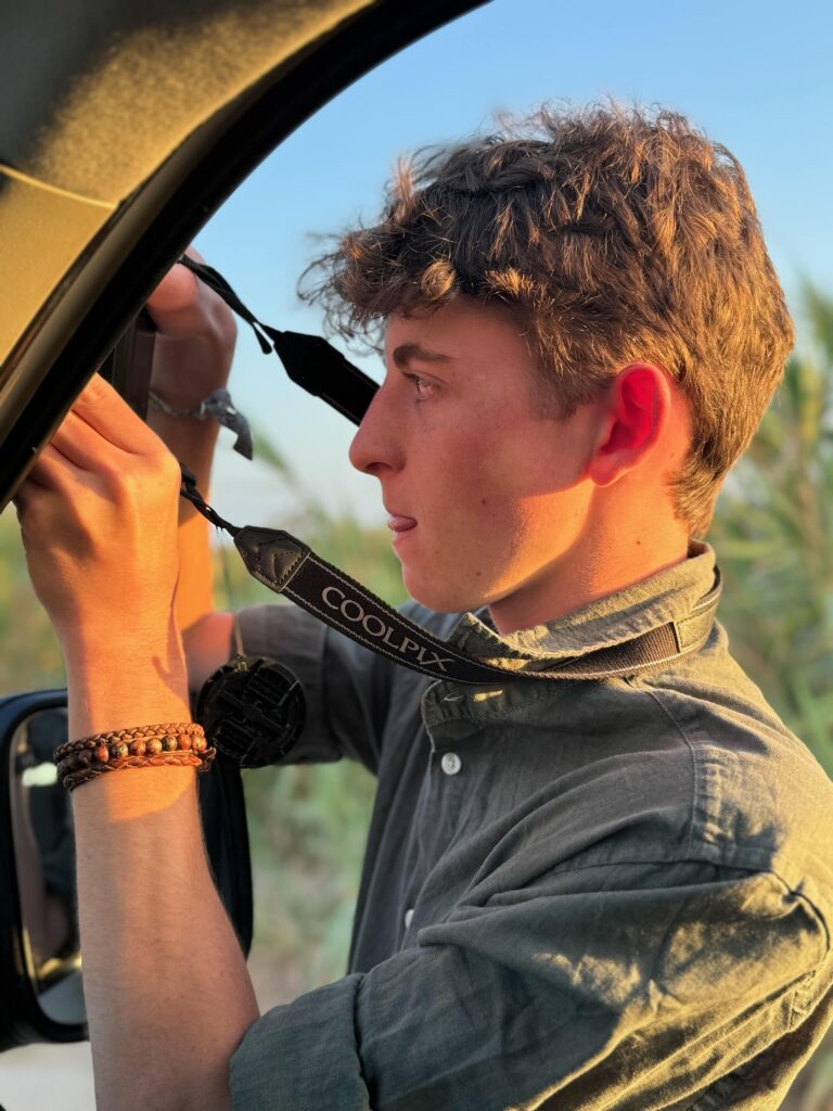 Young man taking photographs of wildlife.  He is wearing a green shirt and looks very focussed with his tongue poking out.