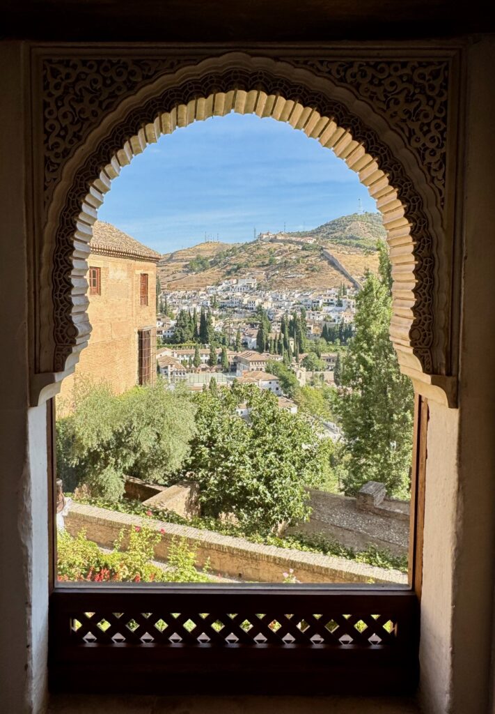 A Moorish arch frames a view out over the surrounding countryside and buildings from inside the Alhambra Palace.