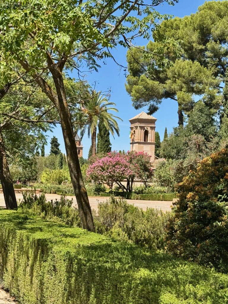 A gorgeous garden vista with wide paths a stone tower rising up amongst the bushes.