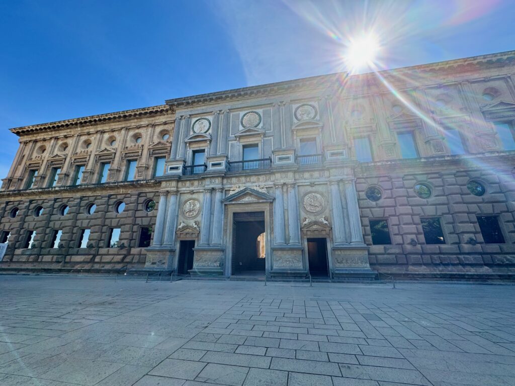 The image is dominated by a huge stone built building with a large entranceway. Sunlight is reflecting off the building.