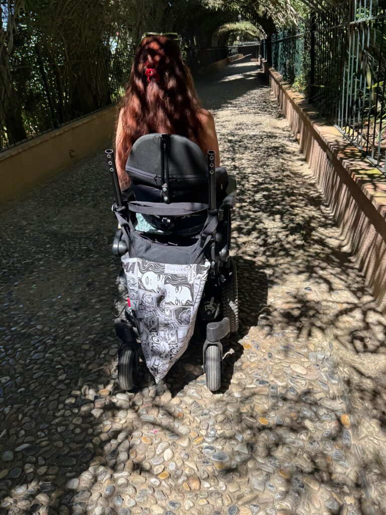 The image shows the path up to the Generalife at the Alhambra - the path is made of small cobbles seen here being navigated by a wheelchair user in an electric chair